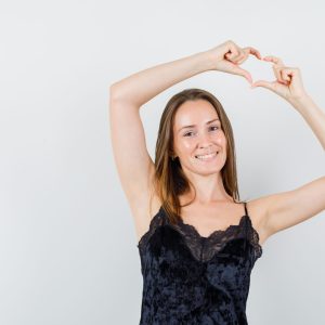 Young female showing heart gesture in black singlet and looking joyful. front view.